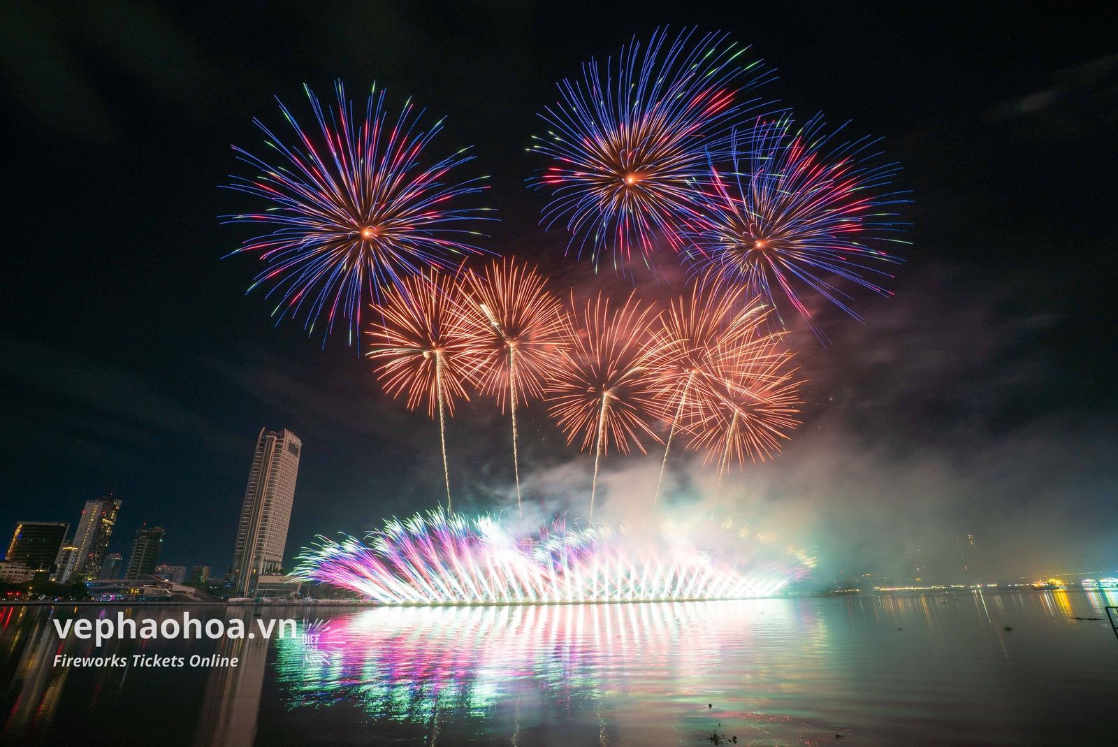 Bầu trời đêm rực rỡ với những chùm pháo bông màu sắc đa dạng, nở rộ trên nền nước phản chiếu ánh sáng. Dưới ánh đèn thành phố, các tòa nhà cao tầng tạo nên khung cảnh đô thị sống động. Hình ảnh mang lại cảm giác sôi động và ấn tượng. Pháo hoa rực rỡ trên sông Hàn, Đà Nẵng, tạo nên khung cảnh tuyệt đẹp vào ban đêm.