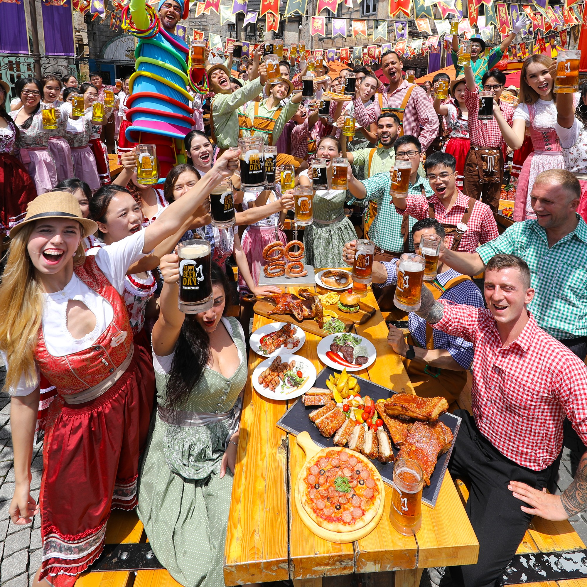 Không khí lễ hội sôi động tại Bà Nà Hills với nhóm người mặc trang phục truyền thống, cùng nhau nâng ly bia và thưởng thức các món ăn ngon. Bàn tiệc đầy ắp đồ ăn và đồ uống, tạo nên khung cảnh vui vẻ và ấm cúng.