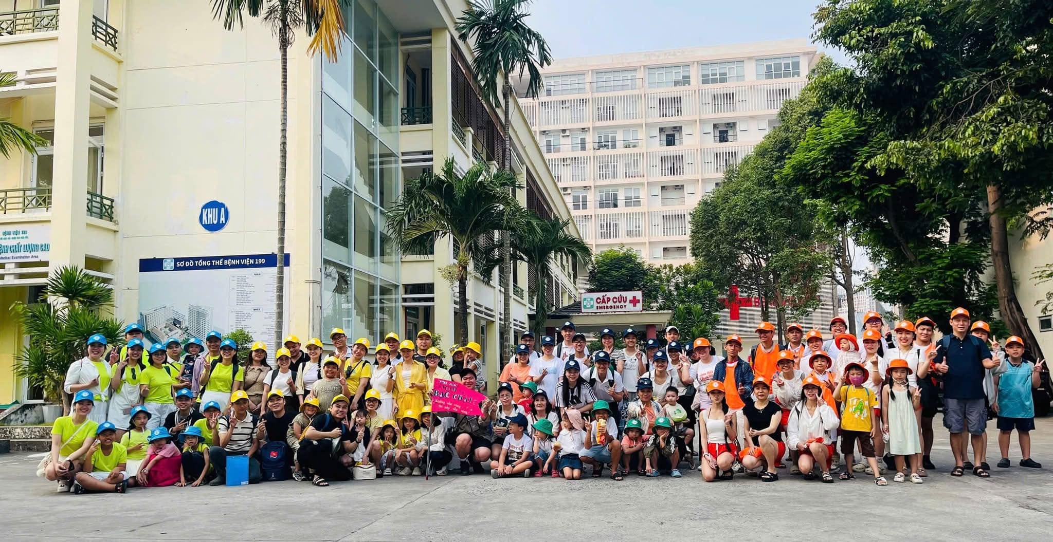 Tour đoàn 100 khách từ Bệnh viện 199 chụp ảnh kỷ niệm tại Núi Thần Tài, với nhiều người tham gia mặc áo đồng phục và mũ màu sắc tươi sáng.