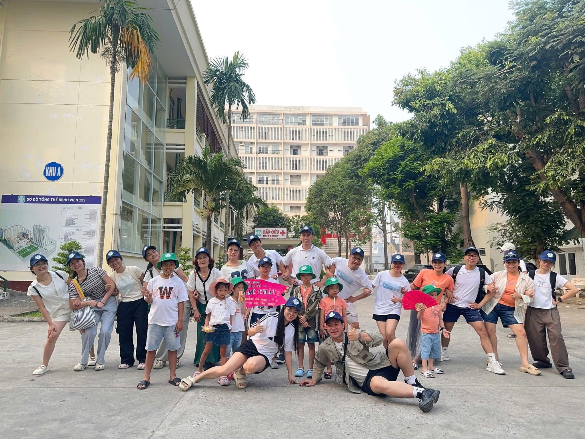 Đoàn khách 100 người từ Bệnh viện 199 chụp ảnh lưu niệm trước khi tham gia tour trải nghiệm Núi Thần Tài, với không gian xanh mát và các thành viên vui vẻ, đeo mũ đồng phục.