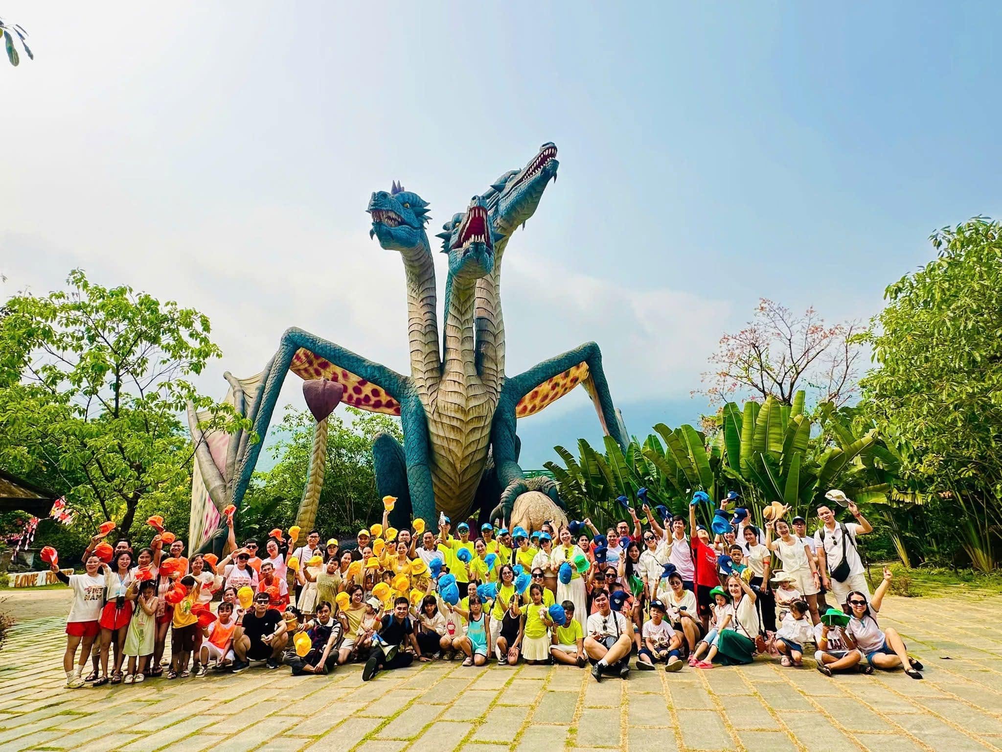 Tour đoàn 100 khách Bệnh viện 199 chụp ảnh lưu niệm tại Núi Thần Tài, bên cạnh bức tượng rồng lớn, với nhiều màu sắc và không khí vui tươi.