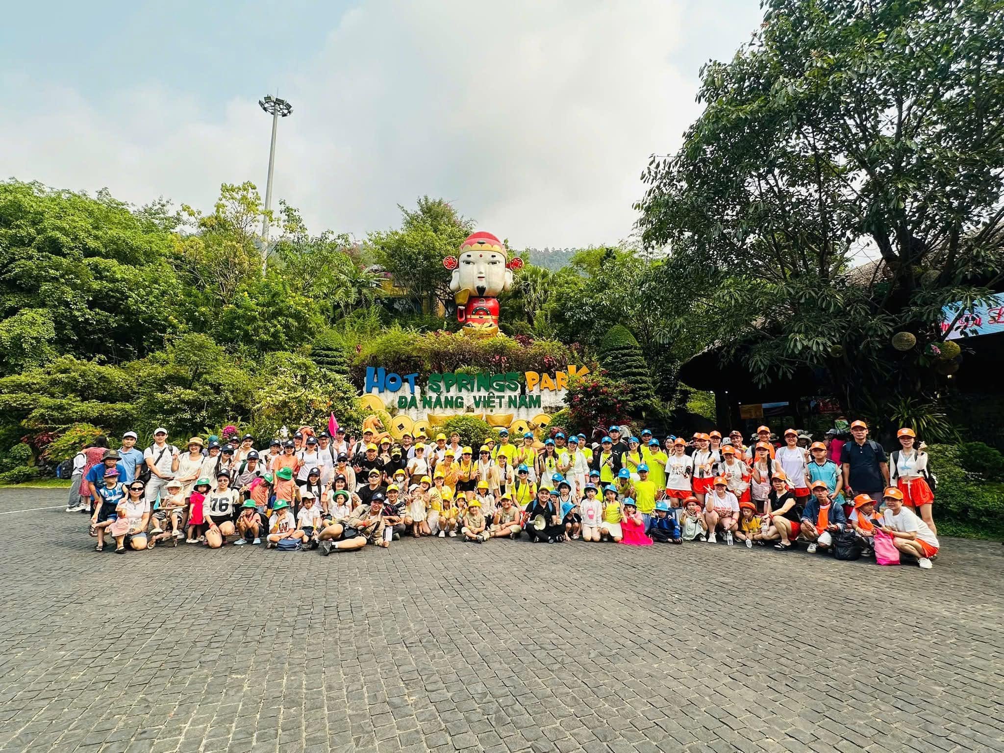 Tour đoàn 100 khách Bệnh viện 199 chụp ảnh lưu niệm tại Núi Thần Tài, Đà Nẵng, với không gian xanh mát và biểu tượng nổi bật phía sau.